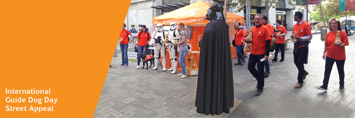 Star Wars Stomtroopers and Darth Vader stand in street with other people in orange t-shirts