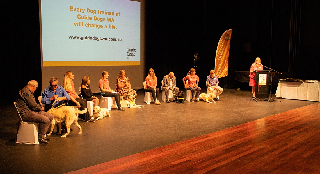 5 graduates and their Guide Dogs and trainers on the stage at the Graduation.