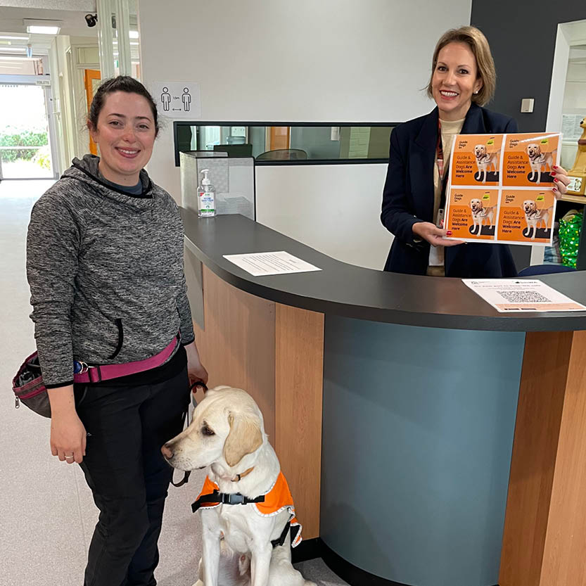 Sticker inside woman at an office reception desk displays guide and assistance dogs are always welcome sticker