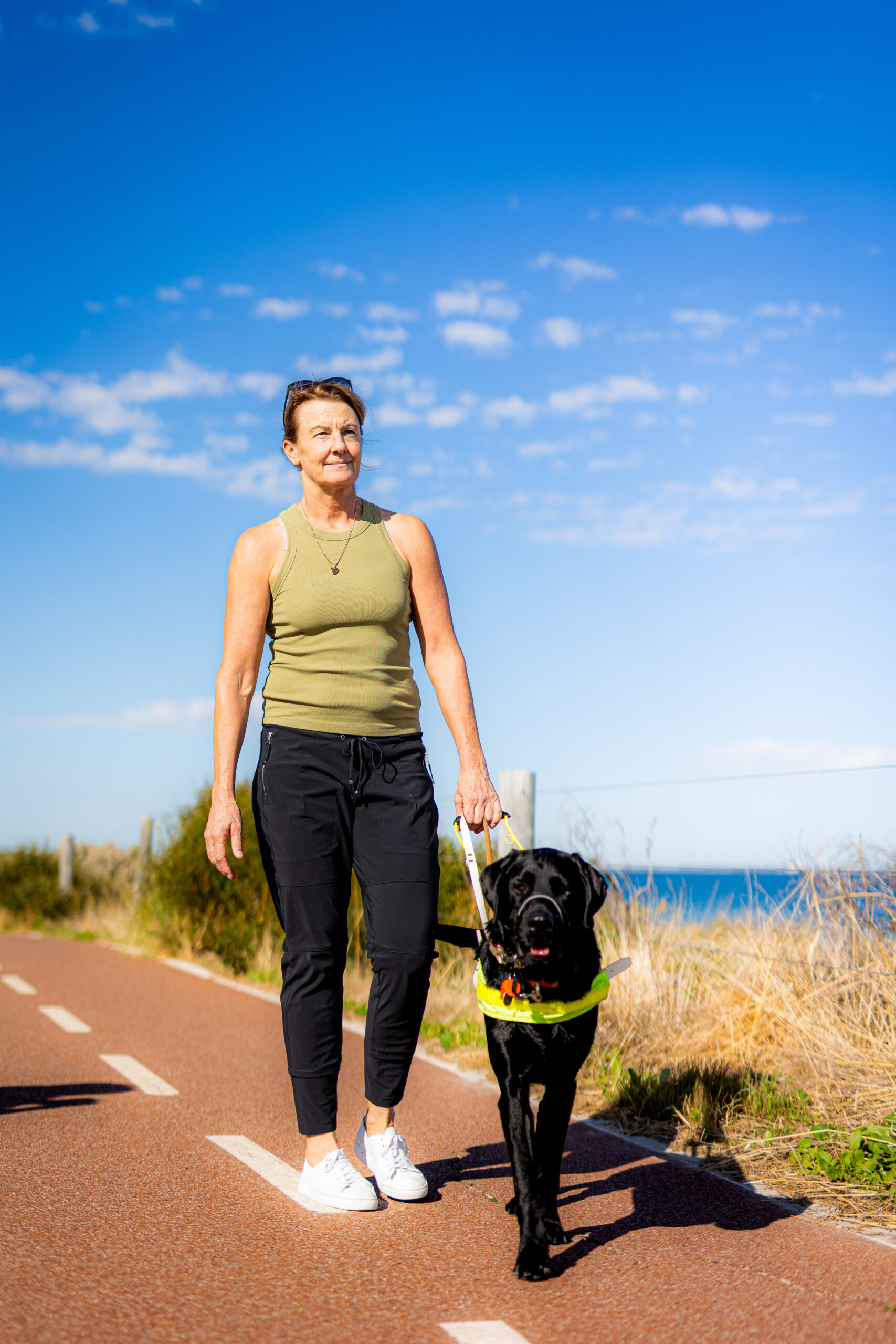 Client Margaret walking with Guide Dog Dalton along a beachside pathway